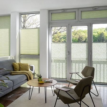 Gemütliches Wohnzimmer mit einer Couch, einem Stuhl und Fensterjalousien, die für eine angenehme Atmosphäre sorgen.