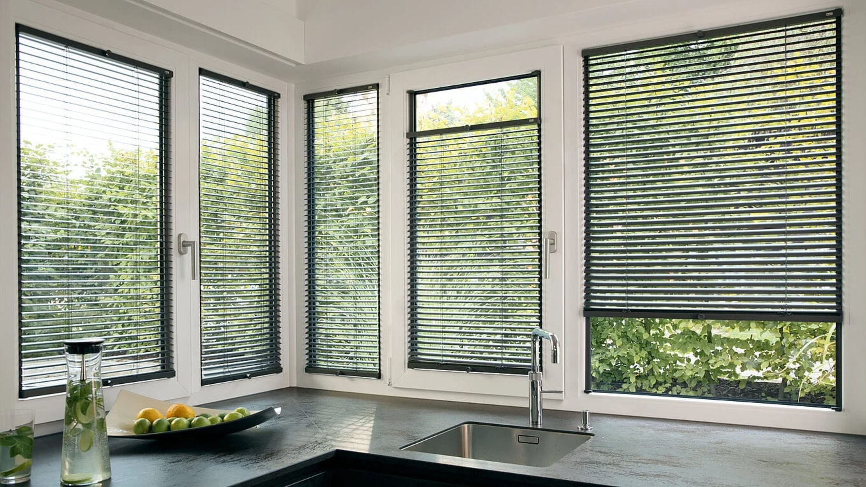 Eine moderne Küche mit schwarzen Arbeitsplatten und Fenstern, die mit Jalousien dekoriert sind.