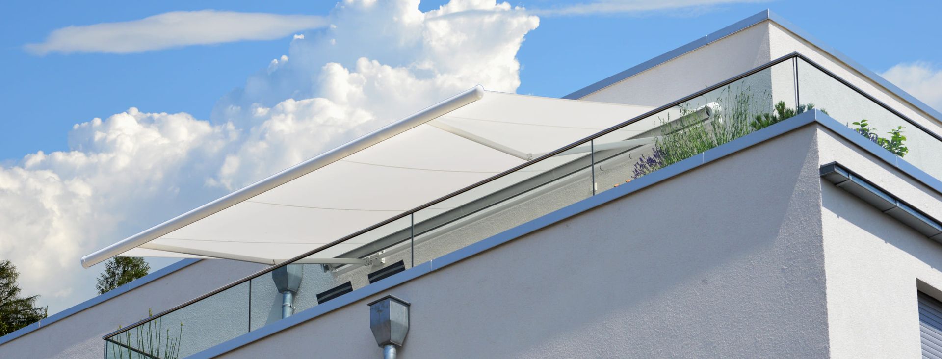Weißer, ausgefahrener Sonnenschutz über Balkon eines modernen Hauses